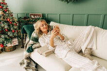 A woman lying on a couch in christmas uses a mobile phone.