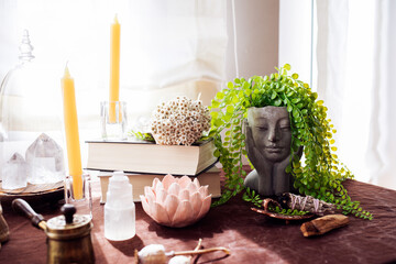 Still life with a cement pot with a woman's face and green hair, books, a bouquet of dried flowers, two quartz stones and a bundle of sage.