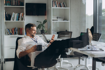 Tired senior manager alone in office drinking coffee and checking news on phone.