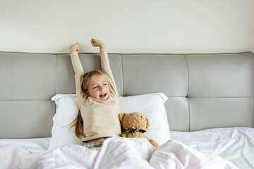 Candid lifestyle portrait of Cheerful caucasian child eight years old in pajamas having fun on bed at cozy home at morning after awake