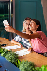 Wall Mural - Portrait of two beautiful women having fun together and chatting in cafe. People smartphone concept