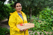 Inspired cheerful successful woman gardener in a yellow raincoat in allotment garden, smiling looking at the camera.