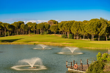 Wall Mural - Golf course located behind the lake with fountains