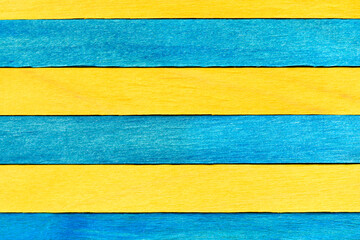 Blue and yellow painted wooden boards. Bright wooden textured background. A wall of alternating blue and yellow wooden planks arranged horizontally.