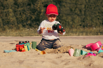 Wall Mural - Child sitting in sandbox playing with toy. Little boy having fun on a playground. Summer outdoor activity for kid. Leisure time lifestyle childhood