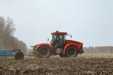 Tractor With Plough Driving On Dry Agricultural Field