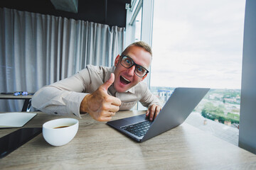 Emotional man looking at the camera at the workplace, a man in glasses, sitting at a desktop with a computer, a student is looking for inspiration for new ideas in an office cafe