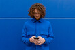 © Bisual Studio/Stocksy - Redhead man using smartphone against blue wall