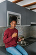 © Ezequiel Giménez/Stocksy - Content black woman with smartphone in kitchen