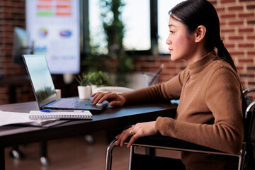 Wall Mural - Wheelchair user planning business project on laptop browser, dealing with chronic health condition. Paralyzed woman with physical impairment working in disability friendly office.