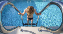 Boy Using Ladder To Enter Swimming Pool.