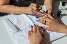 Woman Painting Blue Nails On Another Woman On A White Towel 