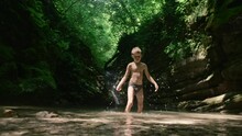 A Child On A Journey. Creative. A Little Boy In Underpants Playing In The Water And Large Rocks From The Cliff Are Visible From Behind.
