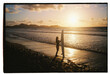 © Berena Alvarez/Stocksy - woman on black sand beach with her surfboard