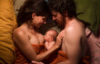 © Ibai Acevedo/Stocksy - Smiling parents enjoying newborn nursing on bed