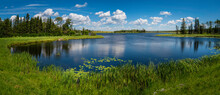Tranquil Landscape And Dramatic Cloudscape With Fur Trees, Water Lily, And Plants In Sand Lake Near Riding Mountain National Park On John Bracken Hwy In Onanole, Manitoba, Canada