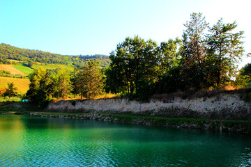 Interesting view from Santarelli lakes in Piane di Moresco with emerald glowing waters contained into a ridge of brazen land with green trees on top and the sun touching gently in the background