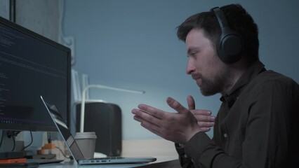 Technology and smart working concept. An IT programmer wearing headphones talks to colleagues working on a computer. Male website developer, software engineer developing an application, video game. 