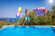 © moofushi - Summer concept with a happy holiday man with hat and sunglasses jumping with two colorful inflatables into a swimming pool