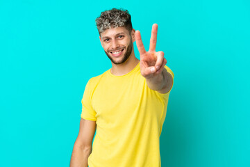 Wall Mural - Young handsome caucasian man isolated on blue background smiling and showing victory sign