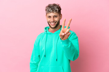 Wall Mural - Young handsome caucasian man isolated on pink background smiling and showing victory sign