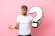 © luismolinero - Young handsome caucasian man isolated on pink background holding a question mark icon and having doubts