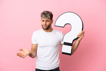 Wall Mural - Young handsome caucasian man isolated on pink background holding a question mark icon and having doubts