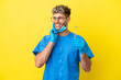 Dentist caucasian man holding tools isolated on yellow background thinking an idea while looking up