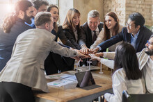 A Group Of Business People Join Hands Around The Office Meeting Table To Celebrate The Success Of A Renewable Energy Project