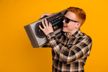 Poster - Photo of young cheerful guy hold shoulder boombox party sound volume isolated over yellow color background