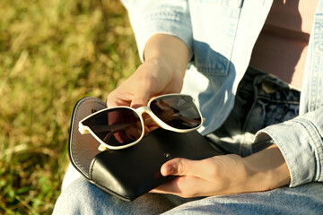 Woman holding sunglasses and case outdoors on sunny day, closeup