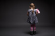 Rear image of a little girl with doll, toddler, offended by someone, being in bad mood, posing isolated over dark grey background.