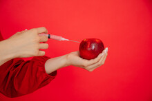 Cropped Woman Hand With Syringe Apply Injection To Fresh Juicy Red Apple In Red Studio. Botox, Hyaluronic Injection Ad