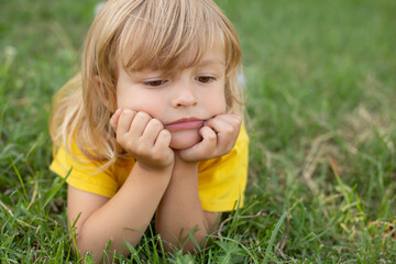 Wall Mural - a blond boy with long hair and a mysterious thoughtful expression on his face lies on a green lawn