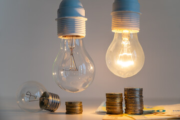 light bulbs, one on and one off, above a pile of coins of increasing height. increases in energy tar