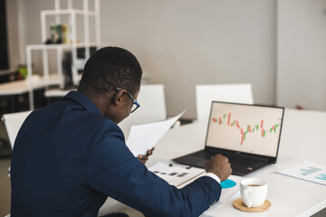 Wall Mural - African American men in a business suit are working on a laptop studying stock market charts and technical analysis.