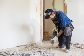 Sticker - Removing a concrete floor with a hand hammer. Concrete rubble on the construction site of a house. Destruction of old tiles. Male construction worker fiercely working in overalls and protective mask.