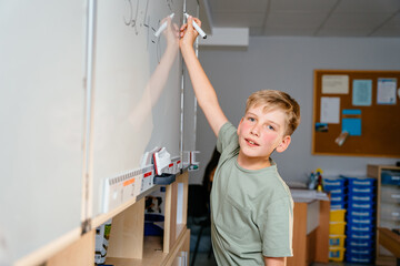 Canvas Print - Cute little smiling schoolboy writing on chalk board at classroom.