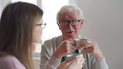 Wall Mural - Adult daughter visiting her senior father at home and having coffee together, talking.