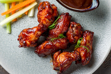 Wall Mural - chicken wings in barbecue sauce on plate macro close up on brown stone table top view