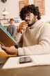 © Drobot Dean - Indian young man wearing eyeglasses reading his note book in cafe