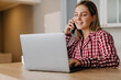 © Drobot Dean - Young happy woman talking on cellphone while using laptop at home