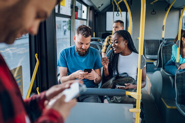 Wall Mural - Multiracial friends talking and using a smartphone while riding a bus in the city