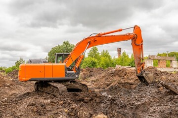 Canvas Print - Orange excavator digs trench in ground against backdrop of green trees and blue summer sky.