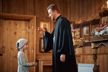 Wall Mural - a priest blesses a little girl in a headscarf in an Orthodox church after a festive church mass