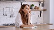 © Stockyana/Wirestock Creators - Caucasian young woman with long red hair writing in a notebook to do list or planning in the kitchen