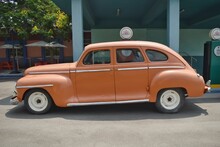 An Old Fashioned American Orange Colored Car Resembling Plymouth De Luxe Near A Petrol Bunk