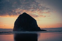 View Of A Large Rock Standing In The Middle Of Sea Or Ocean Shore At Sunset