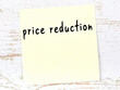 Yellow sticky note on wooden wall with handwritten word price reduction