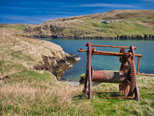 An Abandoned, Rusting Boat Winch With Beach Below In Shetland, UK, Taken On A Sunny Day With Blue Sea In The Background.